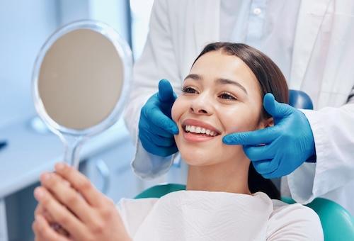 A lady looking at her teeth in the mirror after dental crowns